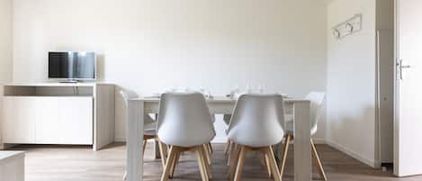A modern dining area with a white table, four chairs, and a television on a stand.