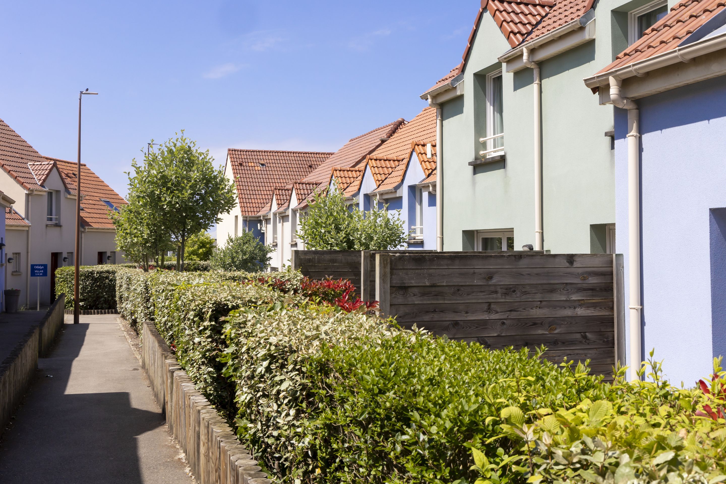 A row of terraced houses with red-tiled roofs, a wooden fence, and a pathway.