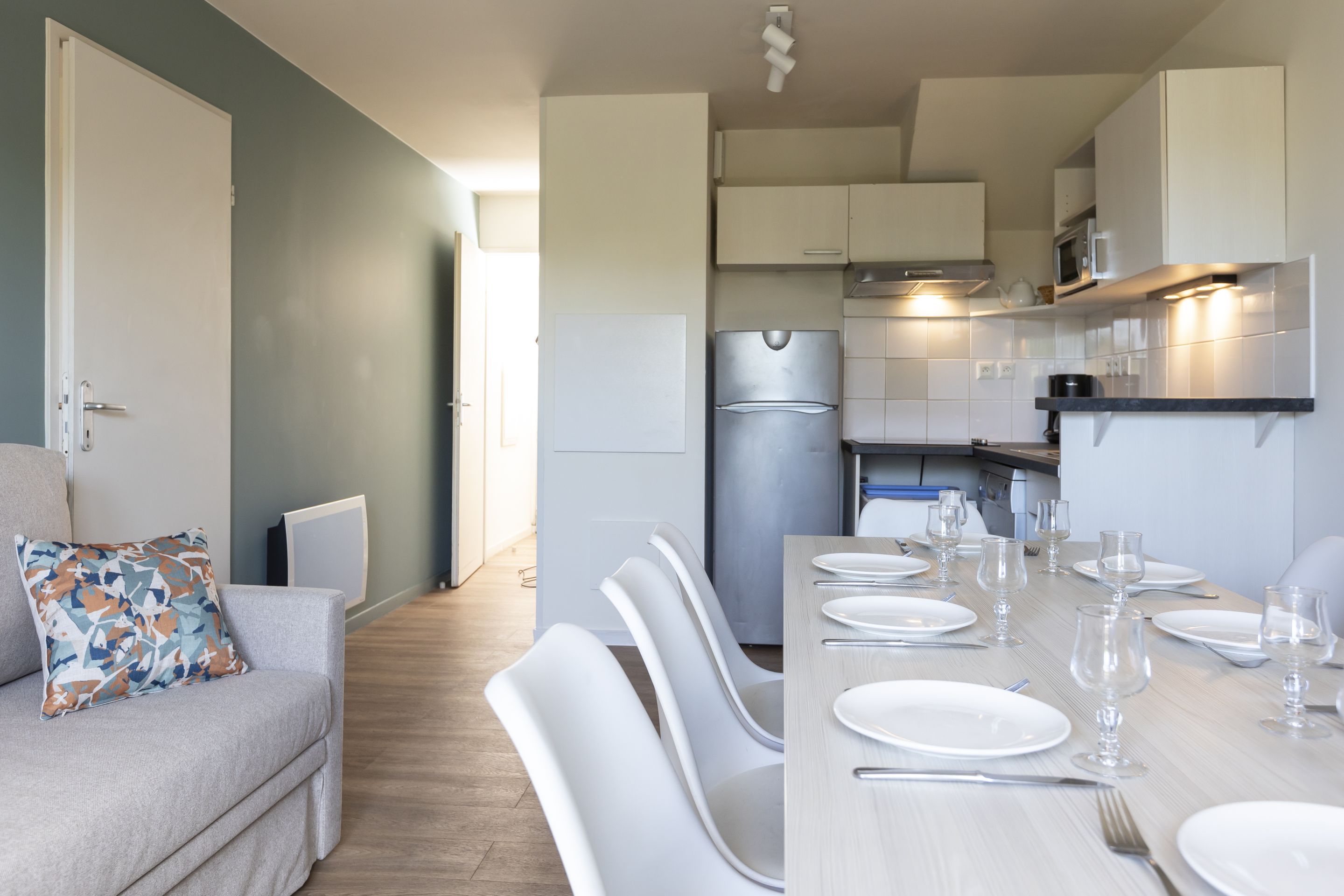 Una cocina moderna con armarios blancos, un refrigerador de acero inoxidable y un comedor con sillas blancas y una mesa preparada para cuatro.