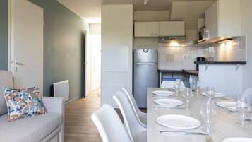 Een moderne keuken met witte kasten, een roestvrijstalen koelkast, en een eethoek met witte stoelen en een tafel voor vier personen.
