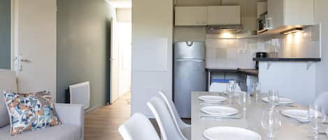 Una cocina moderna con armarios blancos, un refrigerador de acero inoxidable y un comedor con sillas blancas y una mesa preparada para cuatro.