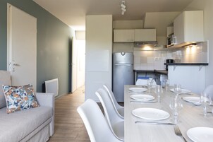 Una cocina moderna con armarios blancos, un refrigerador de acero inoxidable y un comedor con sillas blancas y una mesa preparada para cuatro.