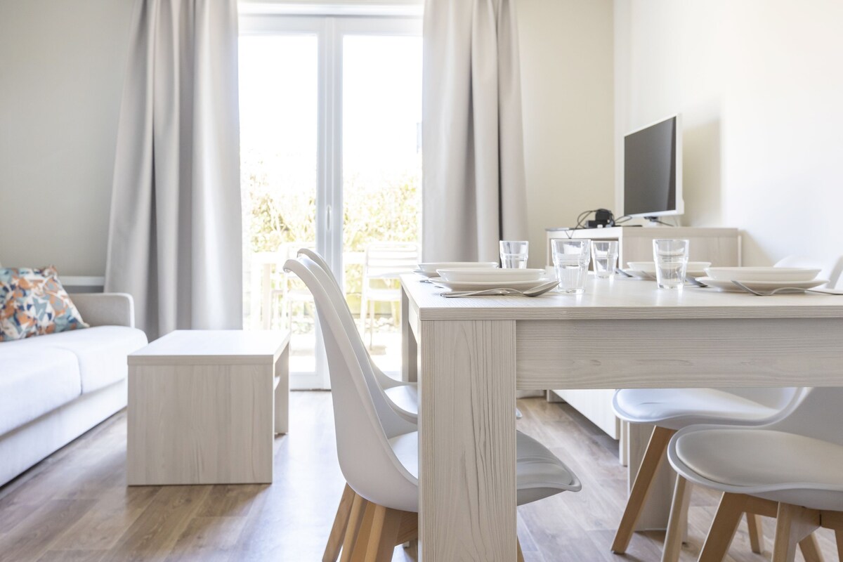 Un comedor moderno con una mesa blanca, sillas y un televisor.