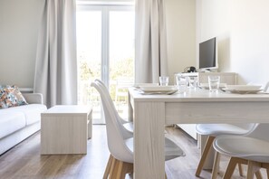 A modern dining area with a white table, chairs, and a television. - Residence Les Villas De La Baie (Le Crotoy)