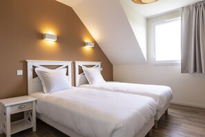 A bedroom with two beds, a nightstand, and a window with curtains.
