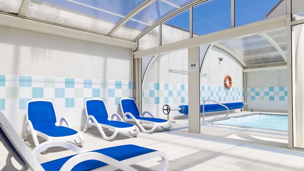 A pool area with blue lounge chairs and a clear glass roof. - Residence Les Villas De La Baie (Le Crotoy)