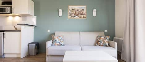 A modern living room with a sofa, a coffee table, and a kitchen area with a microwave.