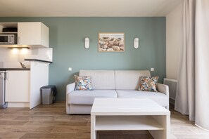 A modern living room with a sofa, a coffee table, and a kitchen area with a microwave. - Residence Les Villas De La Baie (Le Crotoy)