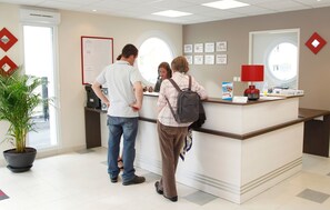 A reception desk with a potted plant, a red lamp, and framed certificates on the wall. - Residence Les Villas De La Baie (Le Crotoy)