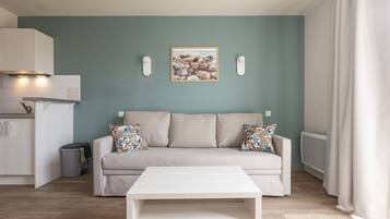 A modern living room with a beige sofa, a white coffee table, and a framed picture of seashells on the wall.