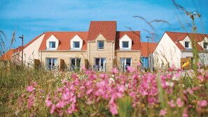 A row of houses with red roofs and white walls, surrounded by a field of pink flowers. - Residence Les Villas De La Baie (Le Crotoy)