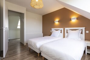 A bedroom with two beds, a wooden floor, a sloped ceiling, and a door leading to another room. - Residence Les Villas De La Baie (Le Crotoy)