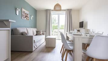 Een moderne woonkamer met een bank, een eettafel en stoelen. Er staat een televisie op een dressoir en een raam met gordijnen.