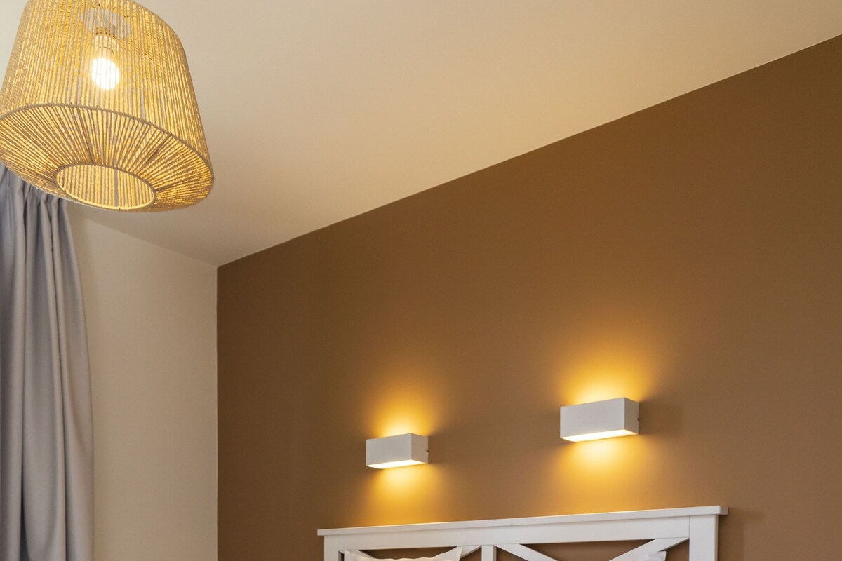 A neatly made bed with white linens, a wooden floor, and two wall-mounted lights.