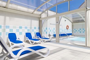A pool area with blue lounge chairs and a clear glass roof. - Residence Les Villas De La Baie (Le Crotoy)