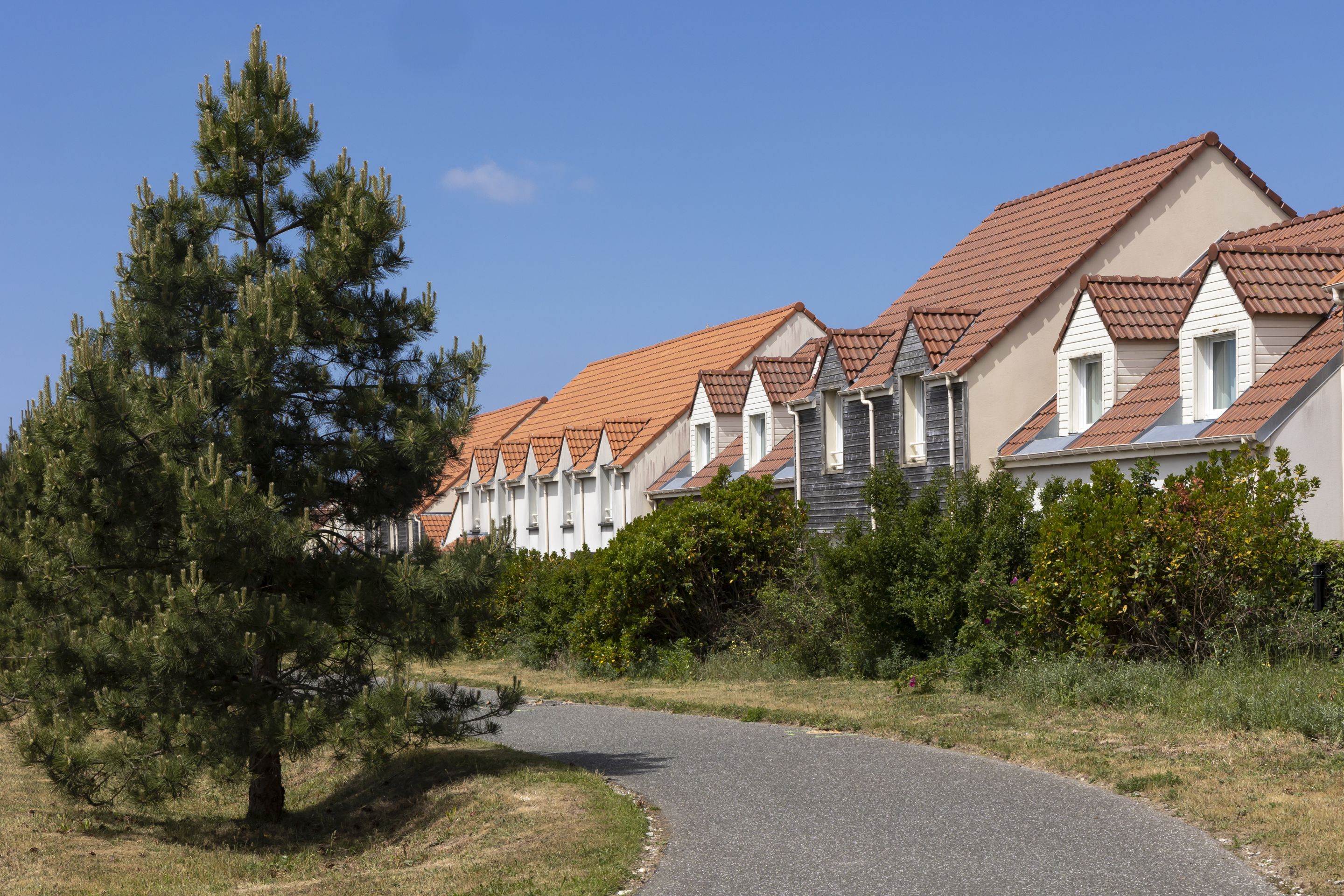 A row of houses with red-tiled roofs and white walls, surrounded by greenery and a curved driveway.
