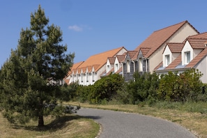 Une rangée de maisons aux toits recouverts de tuiles rouges et aux murs blancs, entourées de verdure et bordées d’une allée sinueuse.