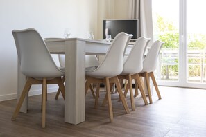 A dining area with a table and chairs, a television, and a view of greenery outside. - Residence Les Villas De La Baie (Le Crotoy)