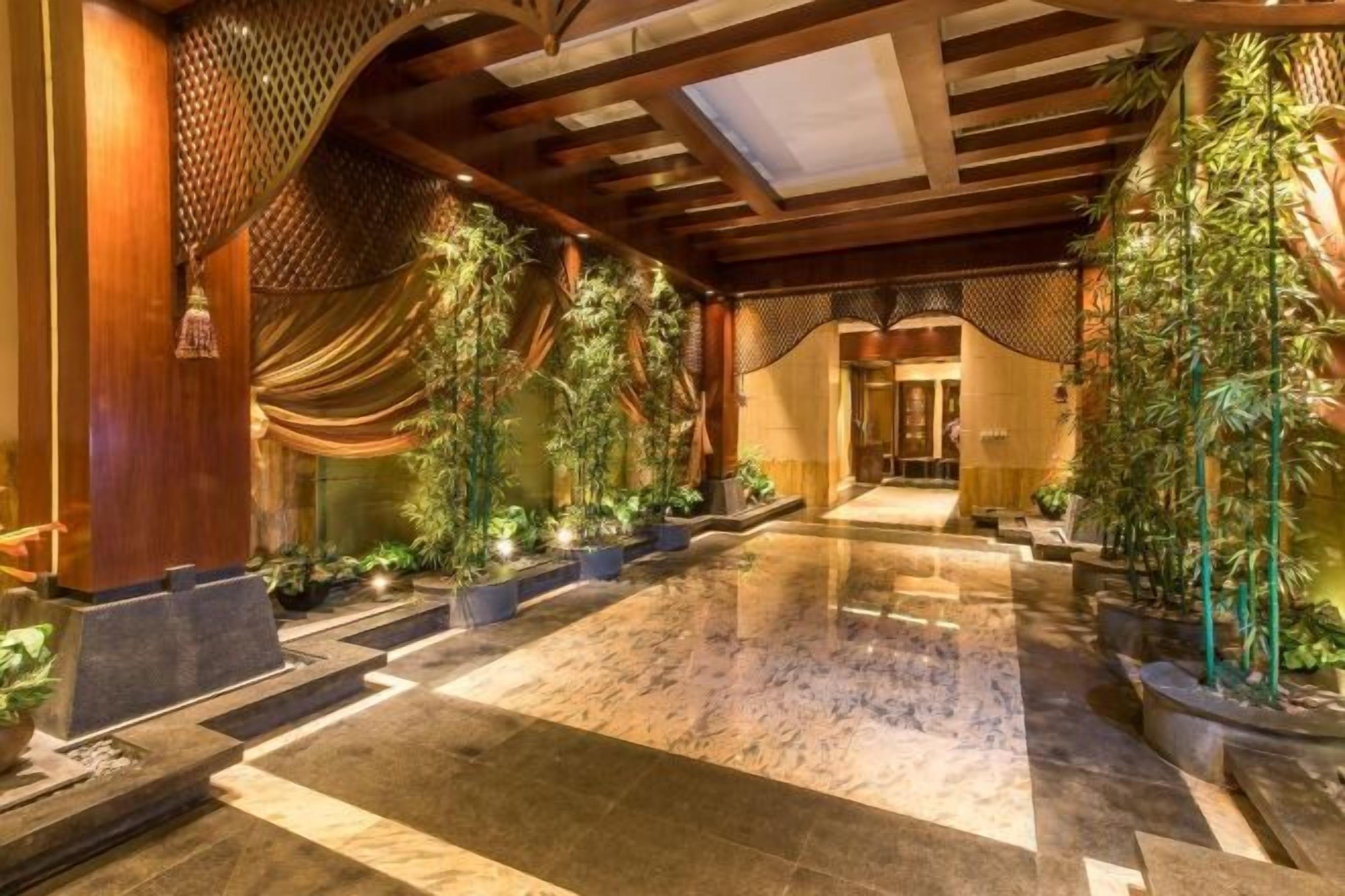 A spacious indoor area with a polished marble floor, wooden beams, and potted plants.