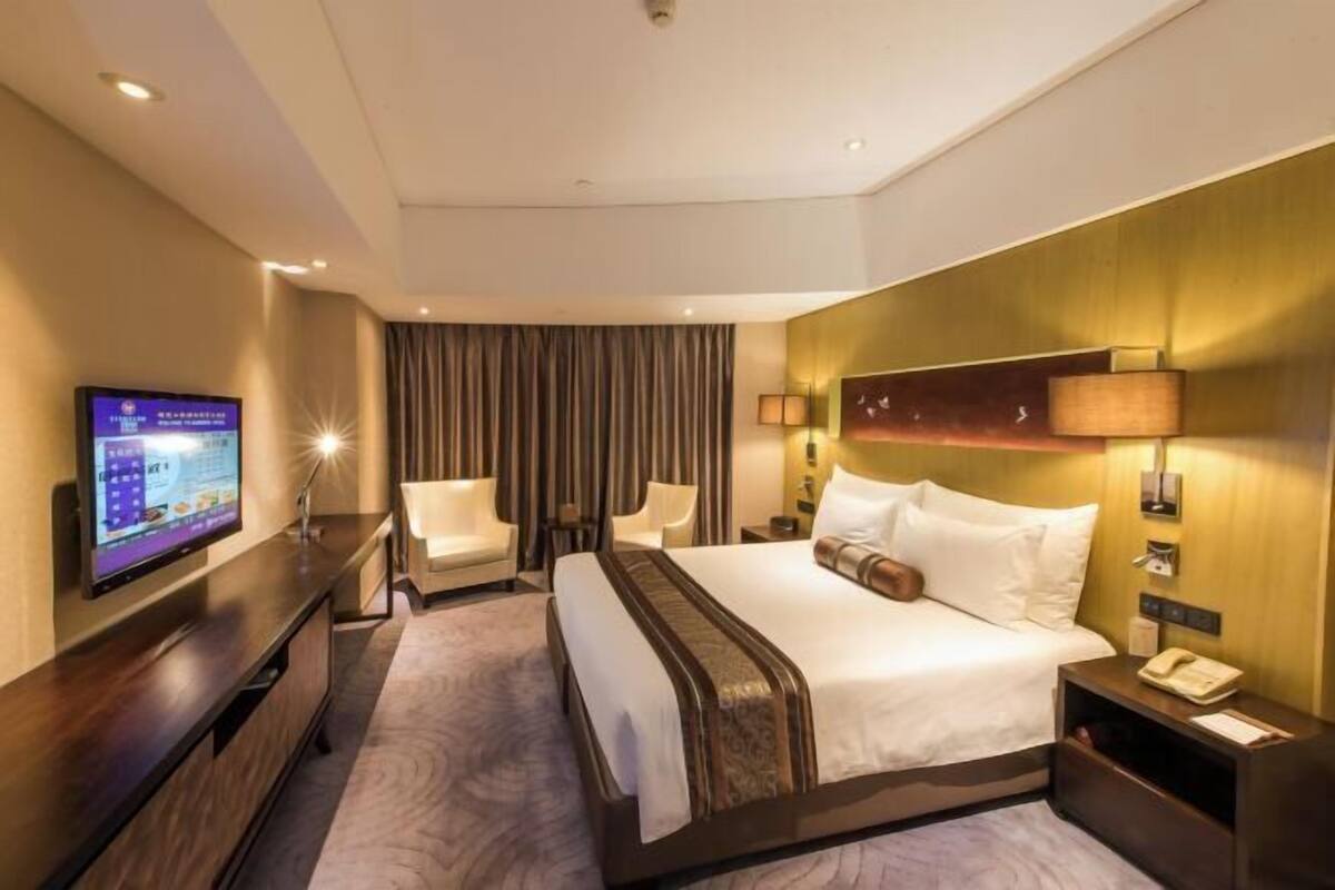 Une chambre d’hôtel avec un grand lit, deux tables de chevet, un téléviseur posé sur un meuble et un rideau à la fenêtre.
