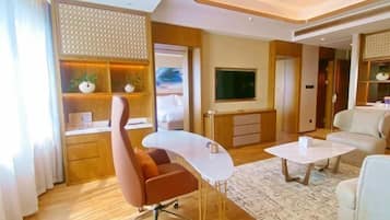 Una habitación de hotel moderna con un escritorio curvo, un sillón cómodo, un sofá, un televisor de pantalla plana y un panel decorativo en la pared.