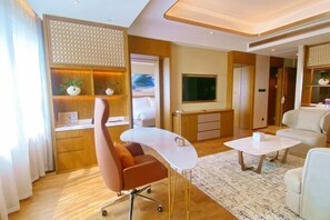 Ett modernt hotellrum med ett böjt skrivbord, en bekväm fåtölj, en soffa, en platt-TV och en dekorativ väggpanel.