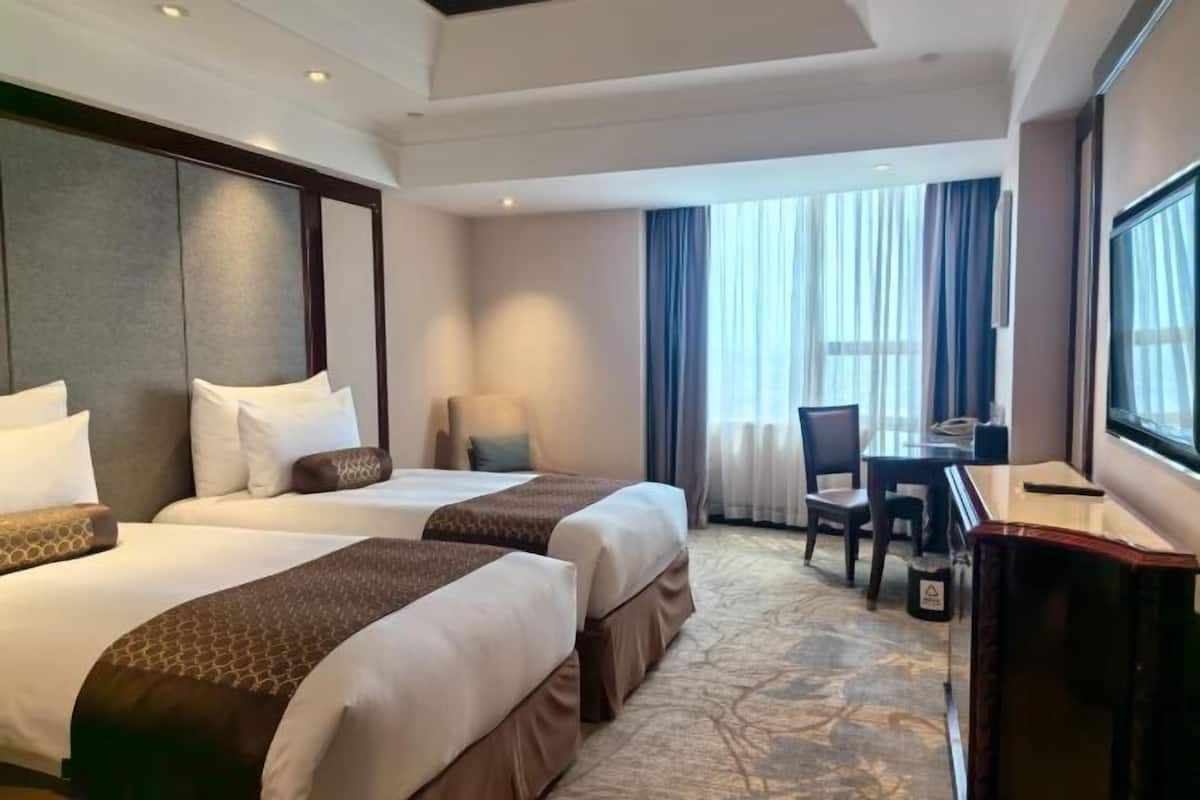 Une chambre d’hôtel avec deux lits, un bureau et une grande fenêtre avec des rideaux.