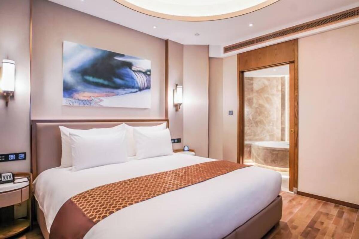 Une chambre d’hôtel moderne avec un grand lit, un tableau accroché au mur et une salle de bain visible à travers une porte ouverte.