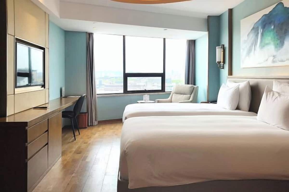 Une chambre d’hôtel équipée d’un lit, d’un bureau, d’une chaise, d’une télévision et d’une fenêtre donnant sur la ville.