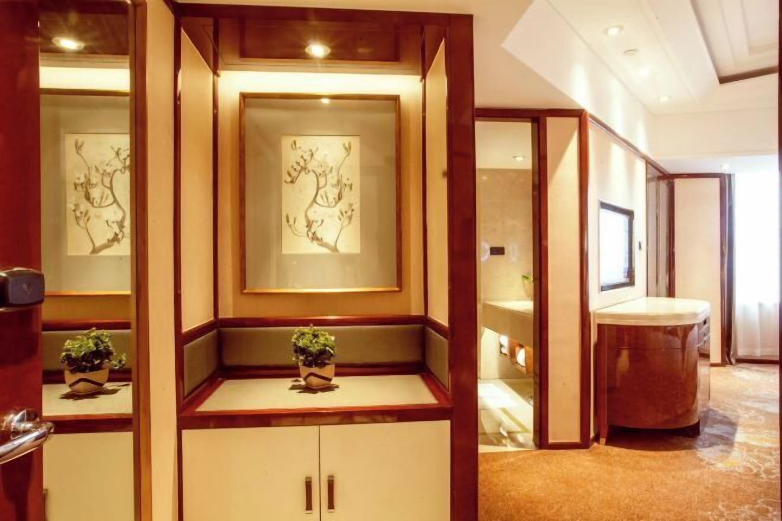 Una habitación de hotel con un armario de madera, una mesita con una planta y obras de arte enmarcadas en la pared.