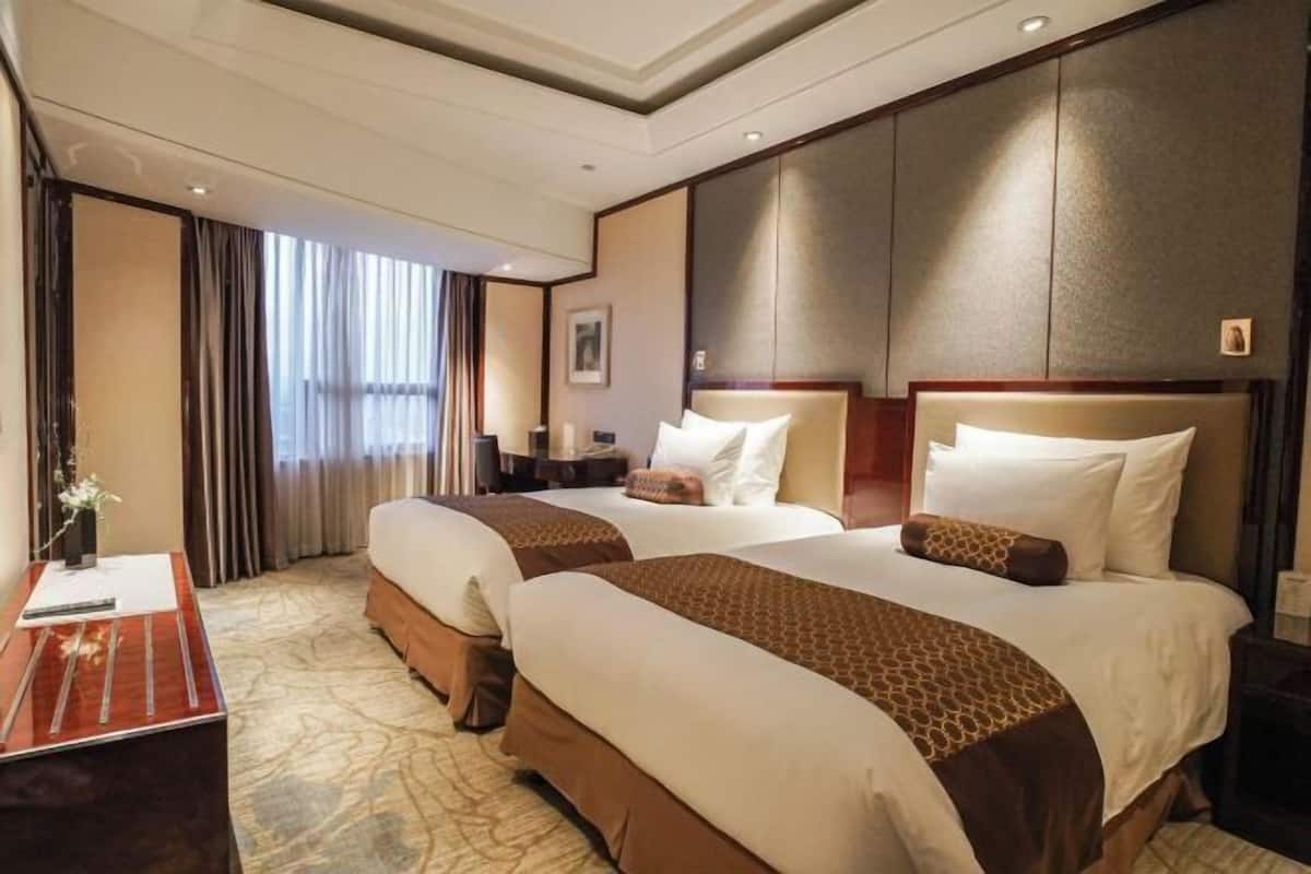 Une chambre d’hôtel avec deux lits, un bureau, une table de chevet et une grande fenêtre avec des rideaux.