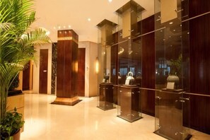 Eine Hotelhalle mit einer Rezeption, Glastrennwänden und einer großen Topfpflanze.