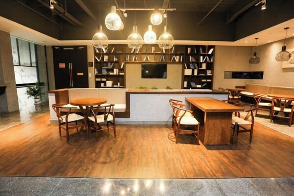 A modern restaurant with wooden flooring, round tables, and hanging pendant lights.