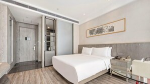 Ein modernes Hotelzimmer mit einem großen Bett, einem Nachttisch, einem Glastisch und einem Kleiderschrank.