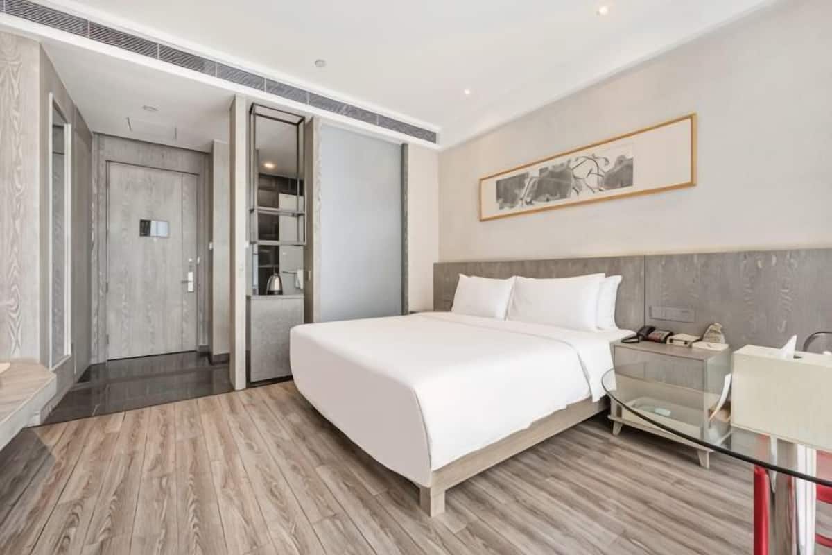 A modern hotel room with a large bed, a bedside table, a glass coffee table, and a wardrobe.