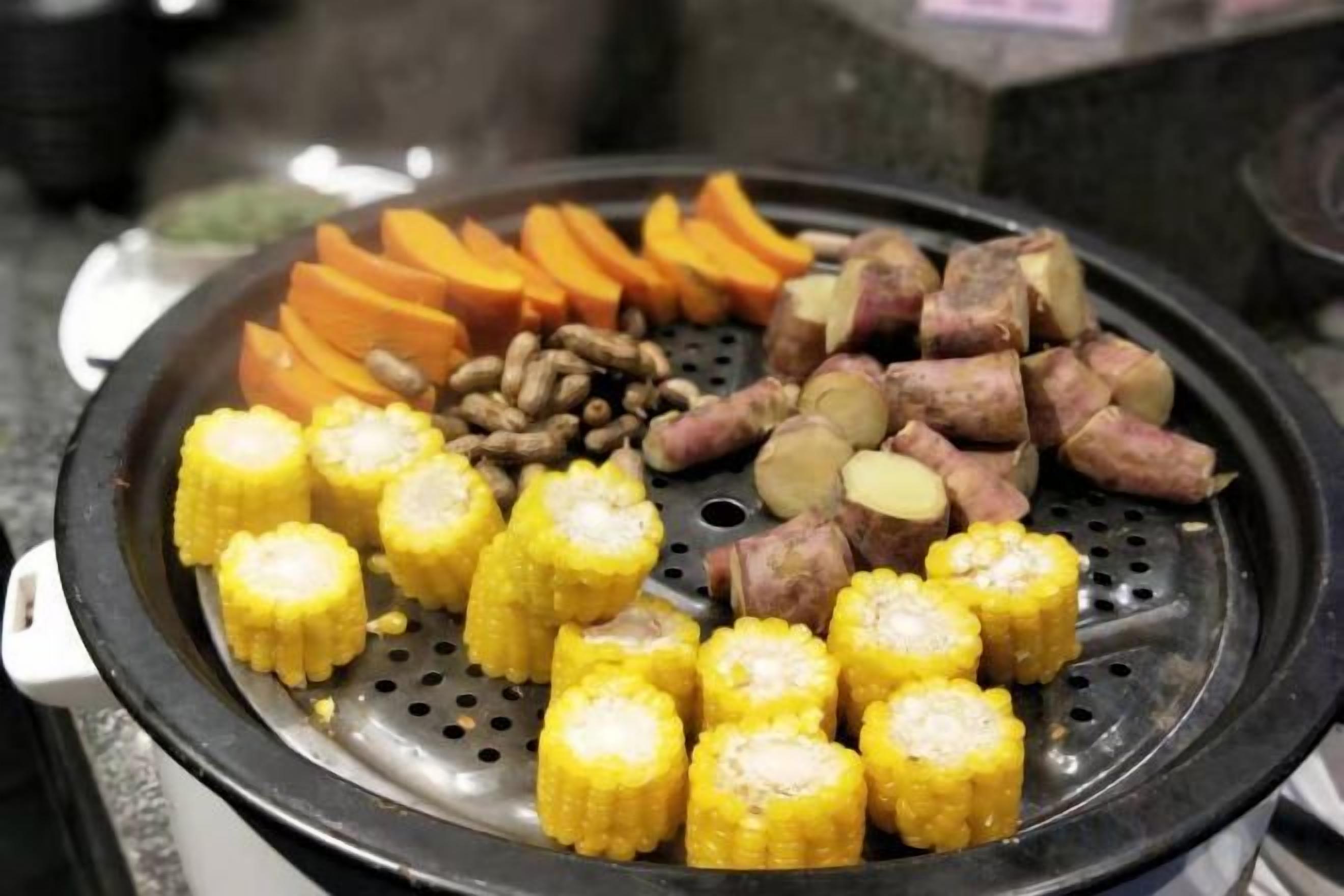 A grill with corn on the cob, sweet potatoes, and sausages.