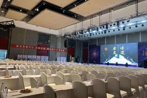 A conference room with rows of chairs, a stage with a large screen, and banners on the walls. - Hotel Select Ankang Lianhua (Ankang)