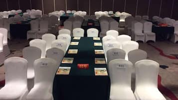 A conference room with rows of white chairs, a long table with name cards, and a carpeted floor.