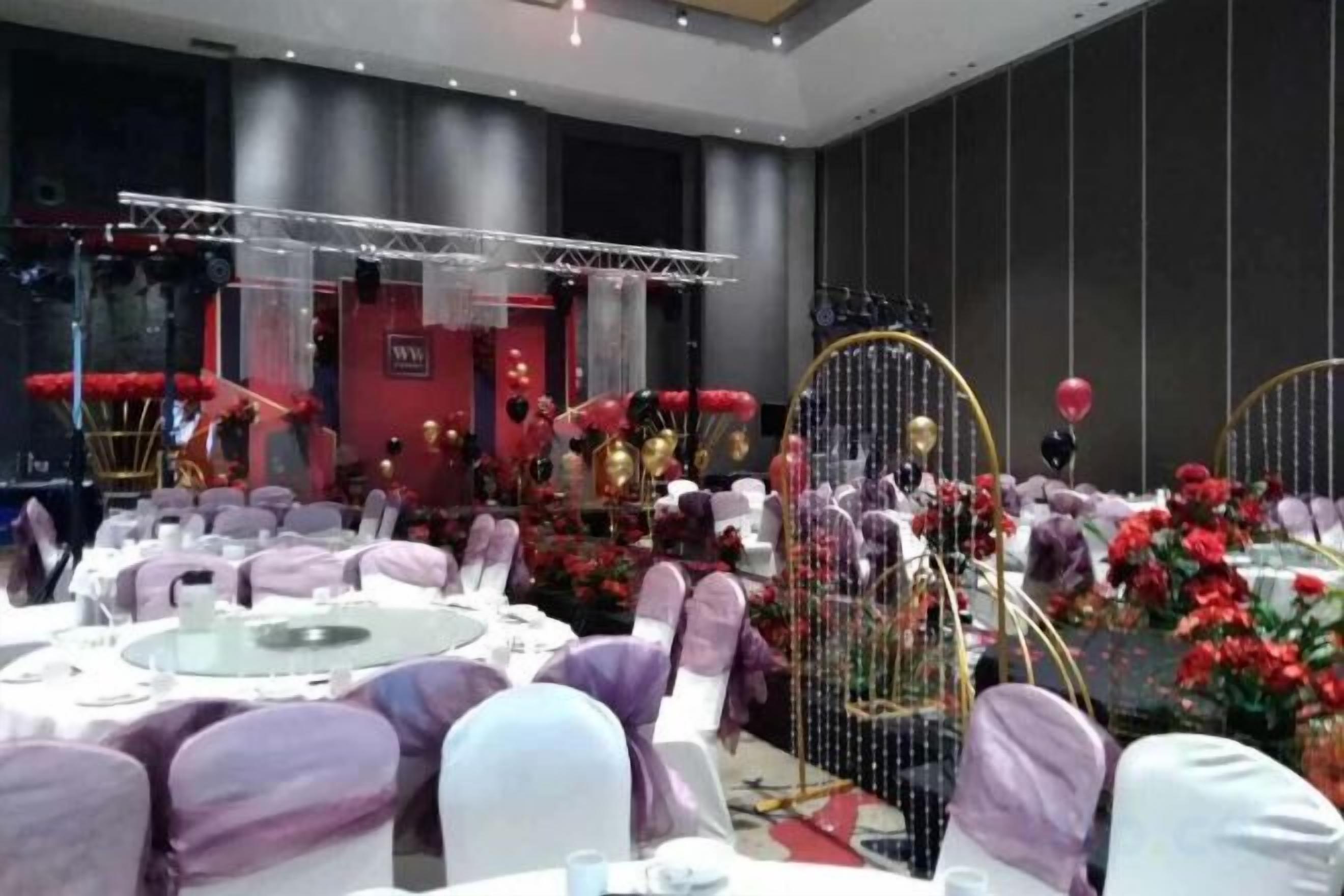 A banquet hall with round tables, chairs, and a stage with musical instruments.