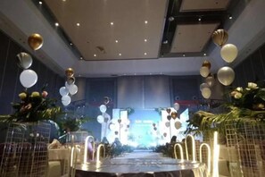 Une salle de banquet avec une longue table, des chaises et une scène dotée d’un décor de fond.