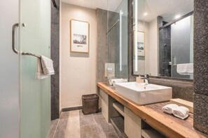A modern bathroom with a glass shower enclosure, a large mirror, a wooden vanity, and a framed picture on the wall.