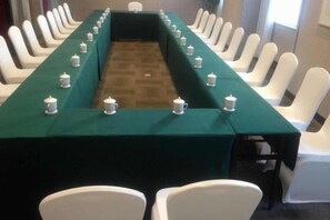 Un salón de conferencias con una larga mesa, sillas blancas y un mantel verde.