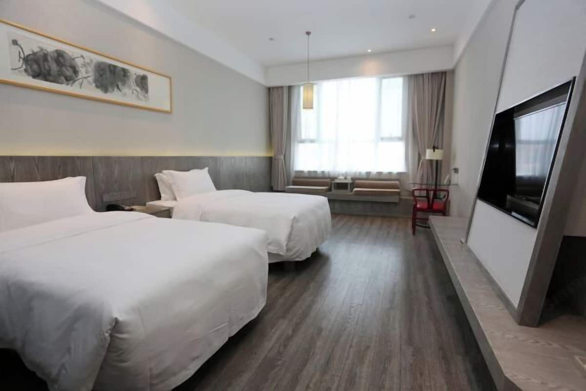 A hotel room with two beds, a TV, a sofa, and a large window.