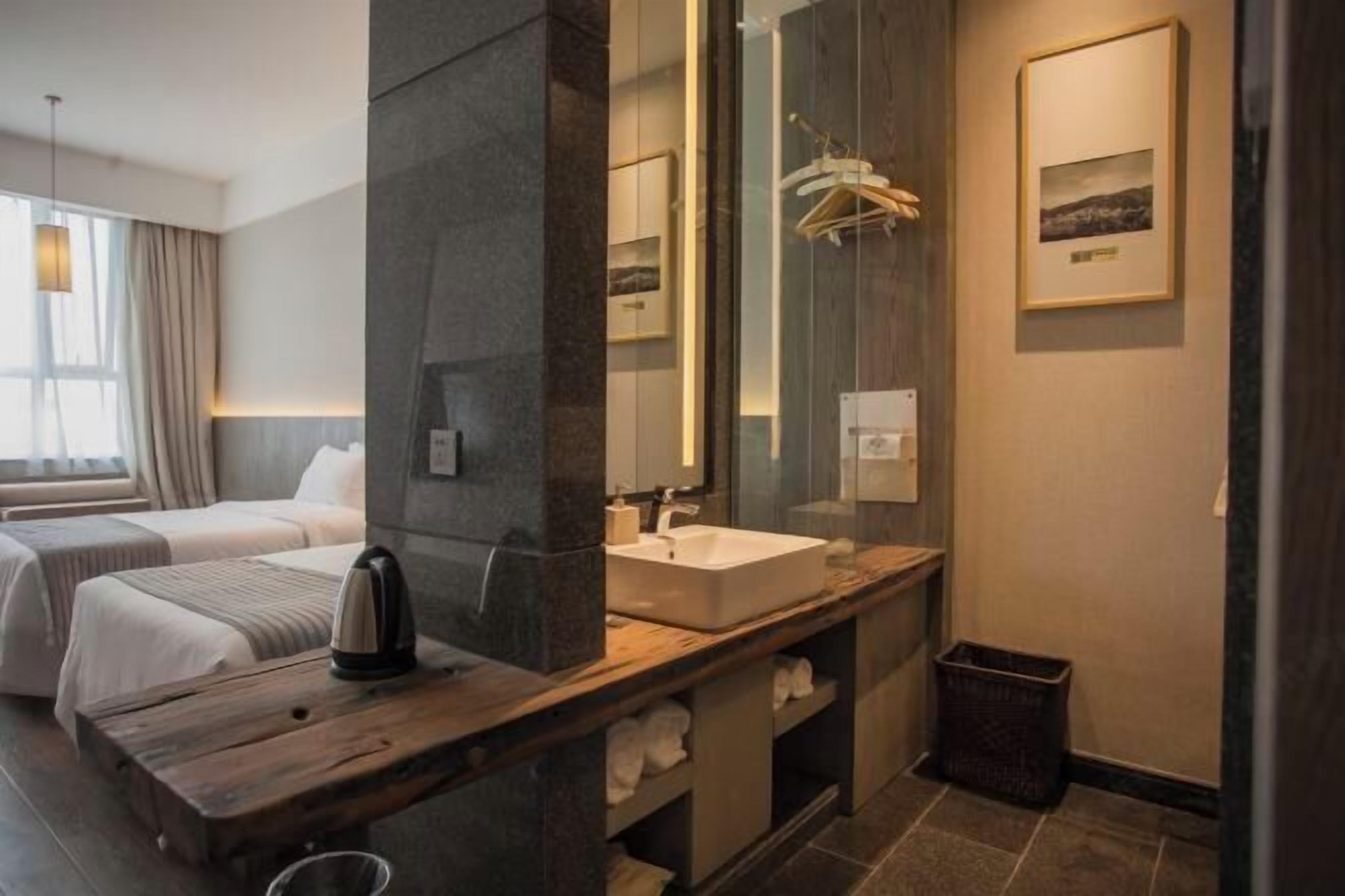 Una habitación de hotel moderna con un espejo grande, un tocador de madera, una cama y una ventana con cortinas.