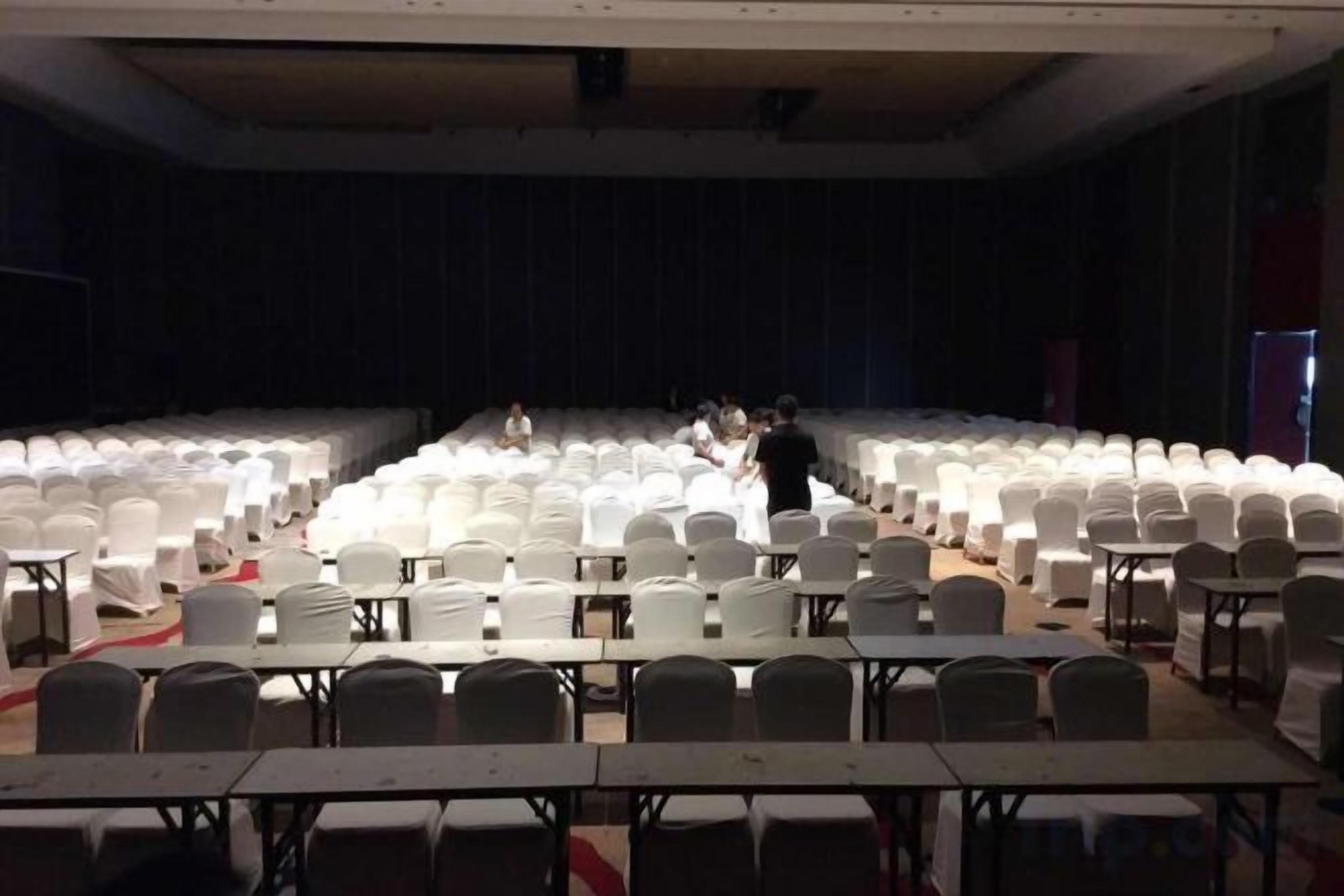 A large hall with rows of white chairs and tables, likely for an event or conference.