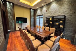 Een vergaderzaal met een lange tafel, stoelen, een televisie en boekenkasten.