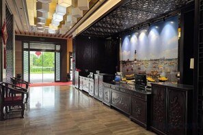 A hotel lobby with a reception desk, a staircase, and a view of a cityscape through a large window. - Laixian Island Hotel (Taizhou)