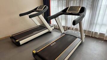 Two treadmills in a room with a window and curtains.