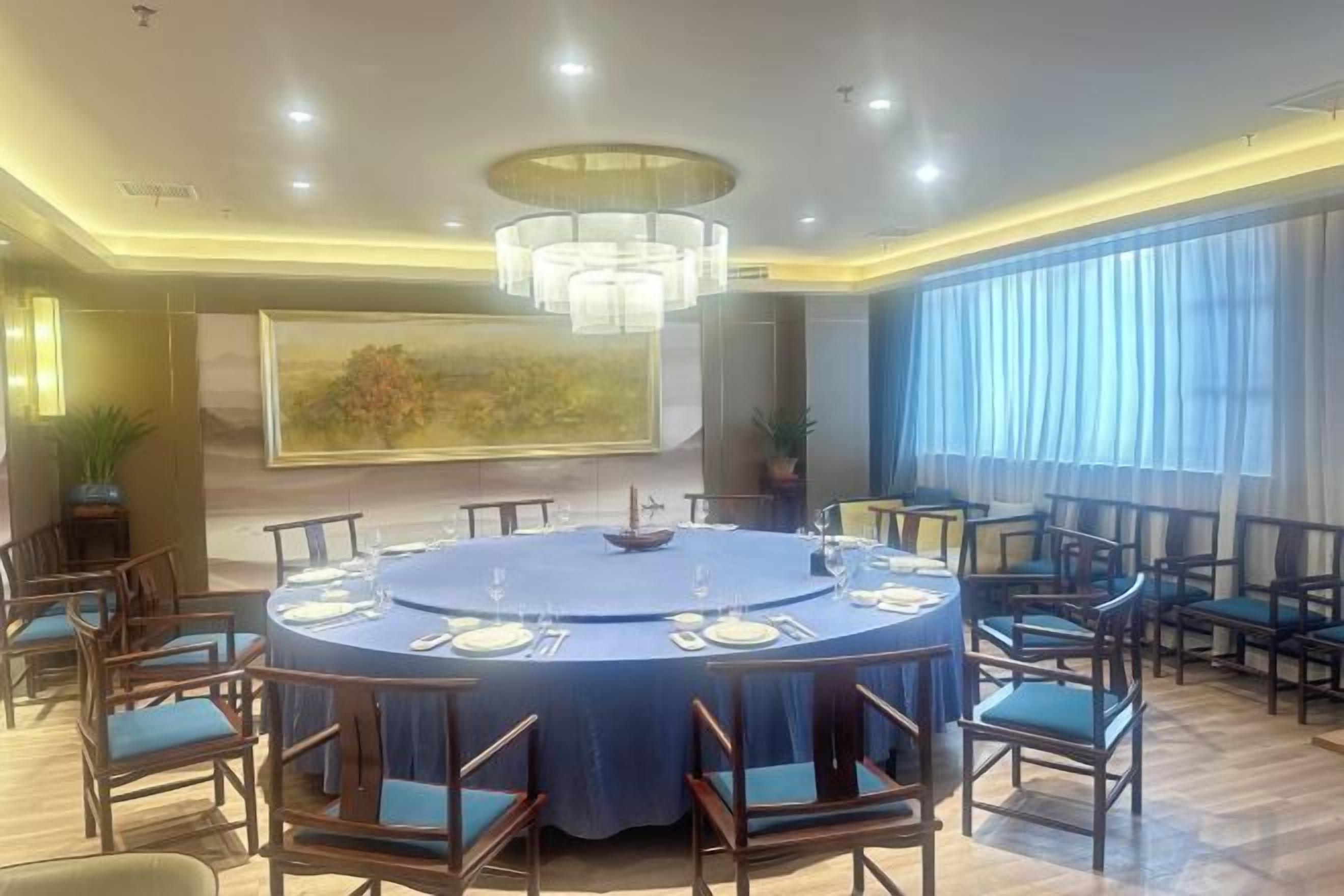 A round dining table with chairs, a chandelier, and a painting on the wall.