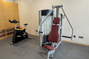 A gym with a stationary bike, a red exercise bench, and a wall-mounted exercise machine. - Laixian Island Hotel (Taizhou)